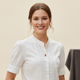 Portrait of Sarah Jenkins smiling warmly, wearing delicate jewelry, against a soft cream background with amber light.